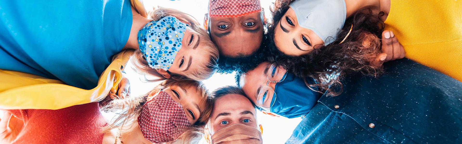 Multiracial group of friends wearing protective face masks taking a selfie - New normal friendship concept with young people looking down at camera and laughing