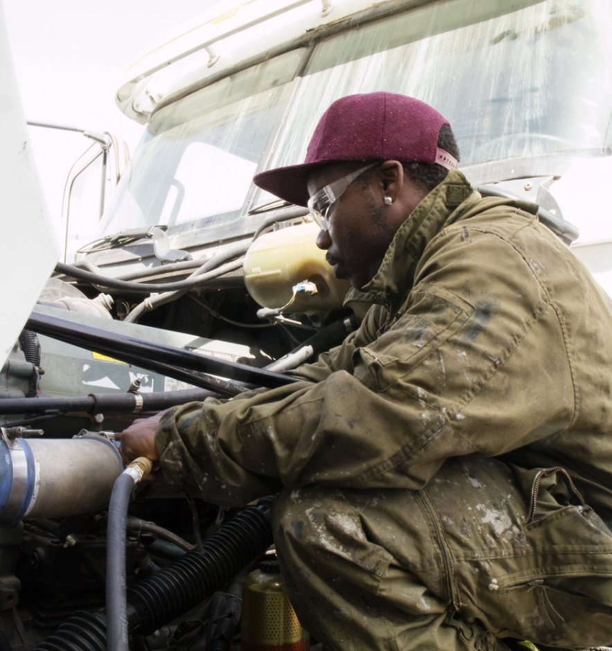 A black man working on the engine of a semi truck.