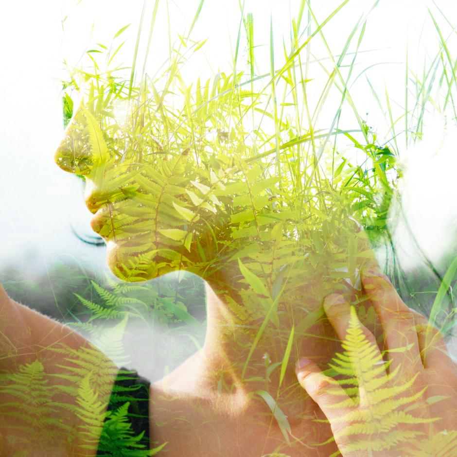 Double exposure portrait of a young, natural beauty with short hair and hand on neck combined with green tropical leaves on an isolated white background