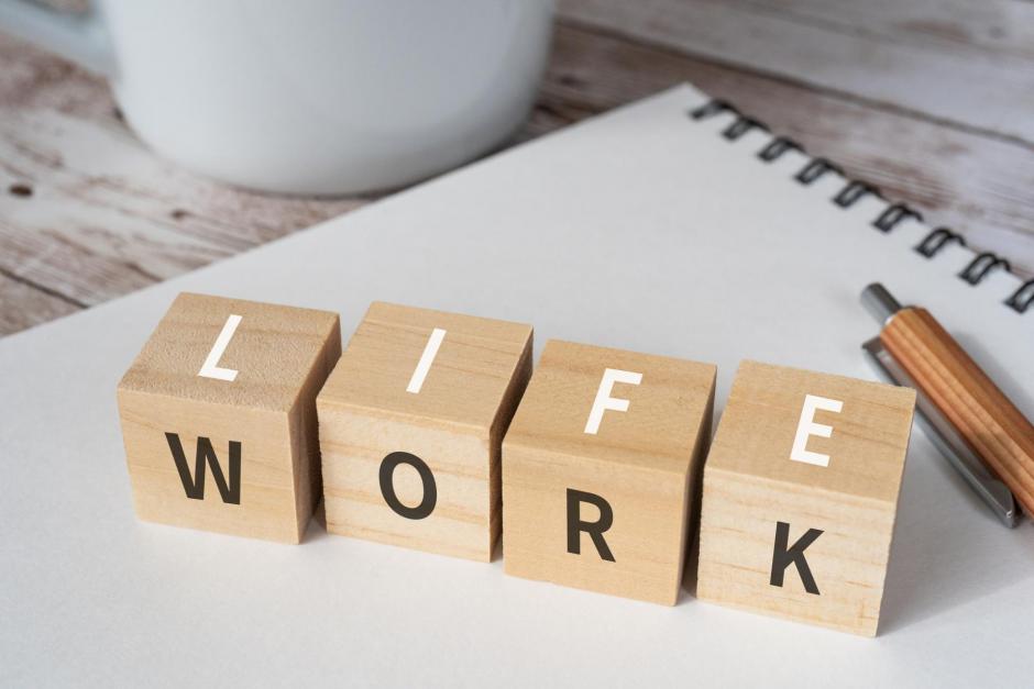 Wooden blocks with "LIFE" and "WORK" text of concept, a pen, a notebook, and a cup.