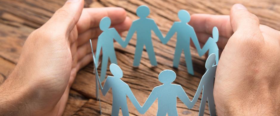 Cropped image of businessman's hands covering paper team on wooden table