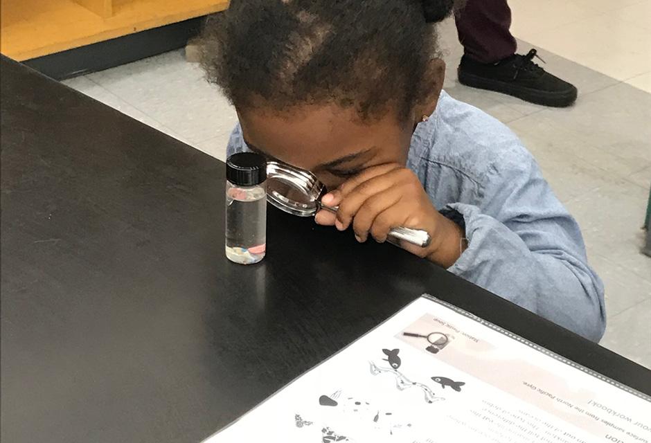A girl examining a bottle with liquid with a magnifying glass at LBCC science night