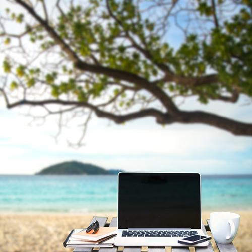 Front view of cup and laptop on table in Office park and blurred background of the beach in the summer