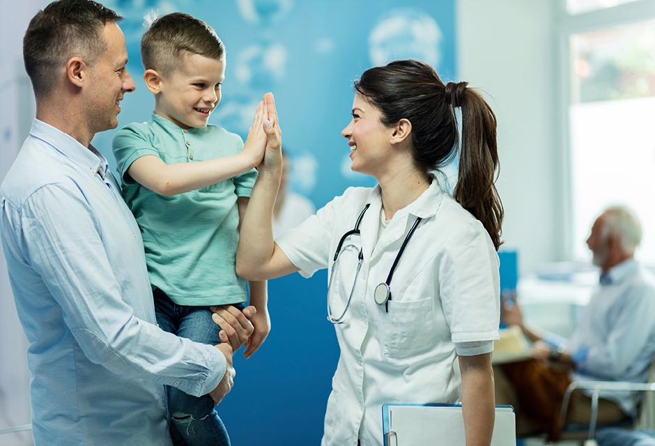 Happy female doctor giving high five to a little boy who came with father at hospital.