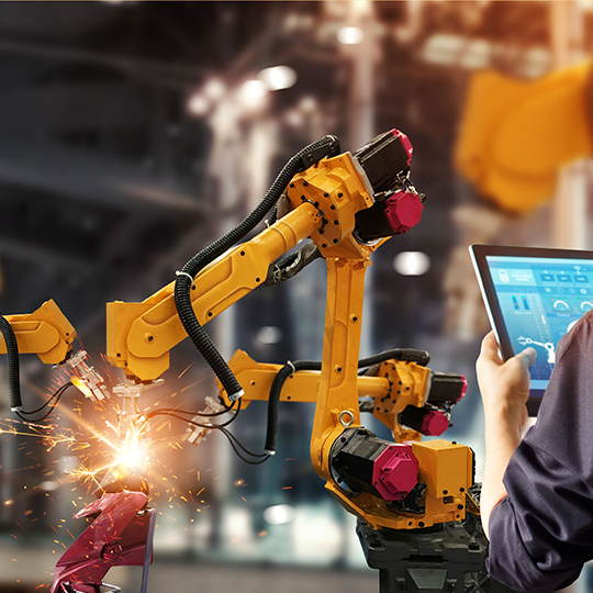 Advanced Manufacturing Technology with robotic arms and technicians operating machines with computer pad